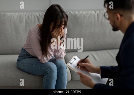 Psicologo maschile che parla con la signora piangente durante la sessione di terapia, dando consigli alla donna araba depressa Foto Stock