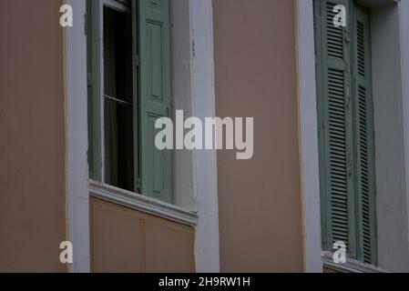 Vecchie finestre in stile neoclassico con persiane in legno verde oliva e finiture bianche contro una parete in stucco rosa veneziano a Nafplio, in Grecia. Foto Stock