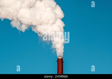 Fumo denso e pesante che esce da un camino arrugginito sotto un cielo blu Foto Stock