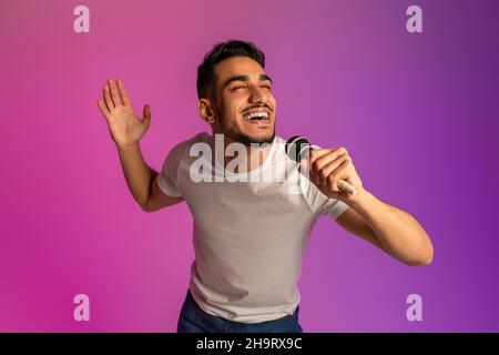 Ritratto di giovane arabo fresco canto canzone, utilizzando il microfono, esecuzione karaoke in luce neon Foto Stock
