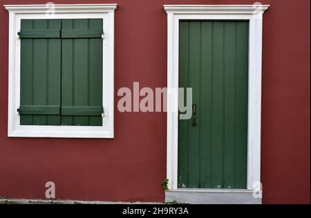 Vecchia facciata tradizionale di casa rurale con una porta di legno di pino verde e finestra con finiture bianche su una parete di stucco rosso veneziano a Nafplio, Grecia. Foto Stock