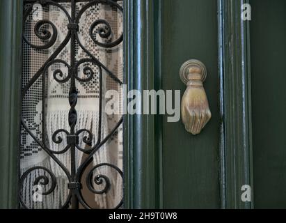 Vecchia casa neoclassica cipresso porta di legno verde con griglie in ferro artigianali, tende in pizzo e un antico bussatore in ottone a Nafplio, Grecia. Foto Stock