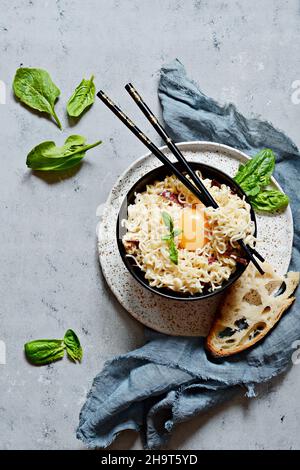 Spaghetti Carbonara con pancetta, tuorlo e salsa cremosa in una ciotola con una fetta di pane ed erbe fresche su sfondo grigio. Pasta di stile asiatico, doshira Foto Stock