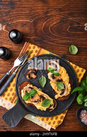 Uova strapazzate con funghi fritti e basilico sul pane su sfondo nero tavolo. Colazione fatta in casa o pranzo con uova strapazzate e funghi Foto Stock