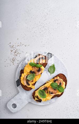 Uova strapazzate con funghi fritti e basilico sul pane su sfondo bianco del tavolo. Colazione fatta in casa o pranzo al brunch. Uova strapazzate e funghi Foto Stock