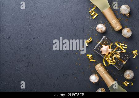 Natale o Capodanno. Confezione regalo per le feste o regalo con nastro, champagne, confetti dorati e baubles d'oro su sfondo nero. Natale Foto Stock