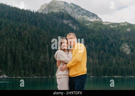 Romantica coppia di nozze in amore in piedi sulla riva di pietra del lago, vista panoramica montagna. La sposa e lo sposo. Bella coppia caucasica abbraccio Foto Stock