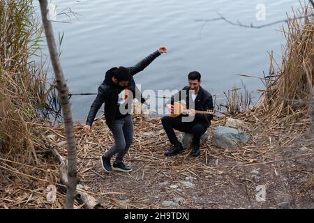 Ankara, Turchia - Dicembre 04 2021: Uomo che suona baglama, strumento tradizionale di musica folk turca e l'altro che balla sul lago. Foto Stock