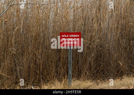 Cartello rosso di avvertimento sul lago: 'E' pericoloso e vietato entrare nel lago' (Göle girmek tehlikeli ve yasaktir in turco) Foto Stock