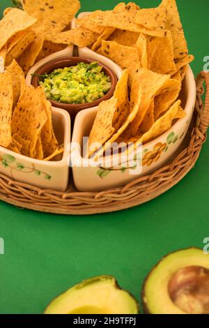 Alcuni nachos fritti in una pentola con qualche guacamole fresco su una superficie verde Foto Stock