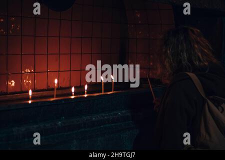 Ragazza che illumina una candela nella chiesa. Candele in preghiera. Foto Stock