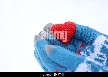 Amore cuore in palme di mani in guanti caldi a maglia contro la neve bianca. Concetto di San Valentino, Natale o carità Foto Stock