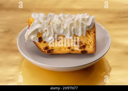 Fetta di panettone con panna montata in piatto bianco su sfondo dorato, tipico dessert di Natale italiano Foto Stock