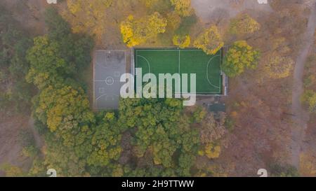 Campo da calcio con erba verde e campo da pallacanestro nel parco cittadino in autunno. Foglie caduta nel parco. Vista aerea. Foto Stock