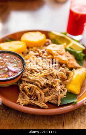 Hornado maiale, un piatto tipico dell'Ecuador che ha anche mote, mais, tortilla di patate e una salsa dolce e salata con pomodoro e cipolla chiamato agrio Foto Stock
