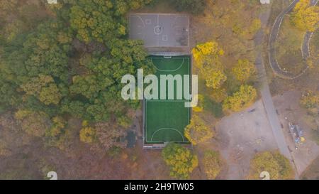 Campo da calcio con erba verde e campo da pallacanestro nel parco cittadino in autunno. Foglie caduta nel parco. Vista aerea. Foto Stock