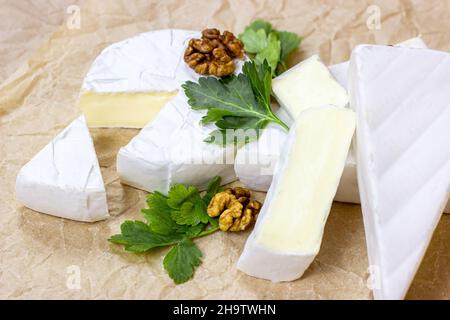 Fettine e cerchi di camembert e formaggio brie con muffa bianca su sfondo di carta chiaro. Foto Stock