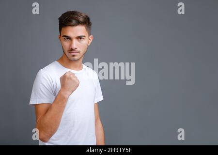 L'uomo in t-shirt bianca mostra un pugno su sfondo grigio Foto Stock