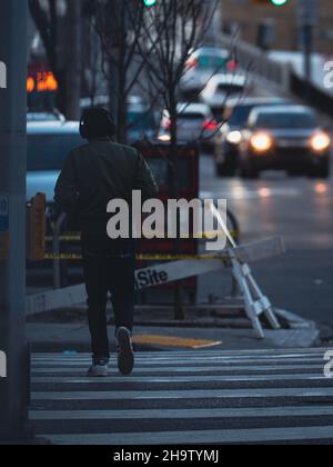 CALGARY, CANADA - Nov 01, 2021: Una vista posteriore di un maschio indossando le cuffie che attraversano la strada nella città di Calgary Foto Stock