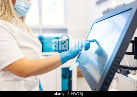 Tecnologia moderna in laboratorio. Un infermiere si trova accanto a una macchina per l'analisi dei campioni di sangue e la programmazione. Un infermiere tocca lo schermo a sfioramento e la p Foto Stock