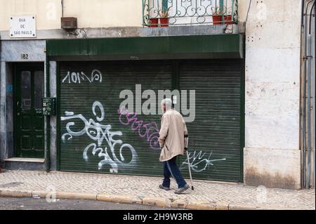 '10.06.2018, Portogallo, , Lisbona - un anziano con un cappello passa davanti a un edificio con graffiti sulle sue persiane nella città vecchia del portogallo capi Foto Stock