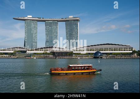 '23.09.2021, Singapore, Singapore - Una tradizionale barca da escursione (bumboat) naviga oltre il Marina Bay Sands Hotel sul Fiume Singapore nel mezzo Foto Stock