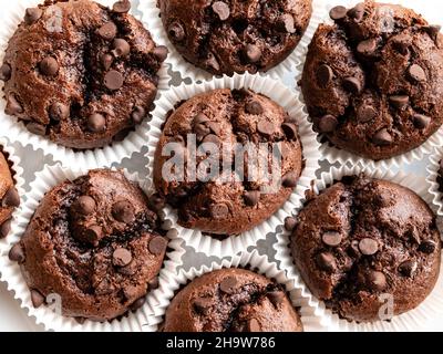 Muffin al cioccolato in una tazza di carta bianca da forno dall'alto. Primo piano di cupcake marroni con gocce di cioccolato. Vista dall'alto, piatto Foto Stock