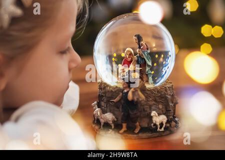 Ragazza che guarda una palla di vetro con una scena della nascita di Gesù Cristo Foto Stock