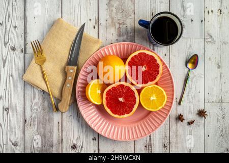 Per colazione, pompelmi e arance deliziose con caffè e posate su tavola di legno bianco Foto Stock