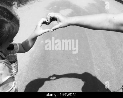 Scatto in scala di grigi di una madre e di un bambino che formano un cuore con le loro mani Foto Stock