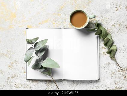 Tazza di gustoso caffè, libro e rami di eucalipto su sfondo chiaro Foto Stock