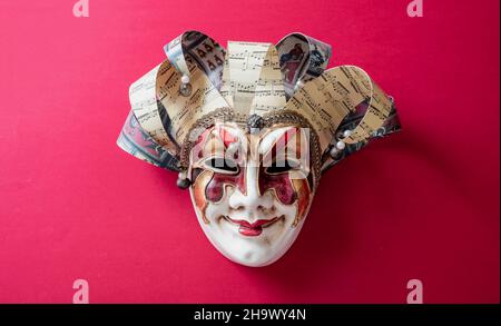 Maschera harlequin veneziana di Carnevale su sfondo rosso. Commedia dell'arte personaggio masquerade. Tradizionale festa travestito, Foto Stock