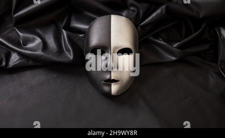 Maschera veneziana a due facce, mezzo nero mezzo argento su sfondo tessile satinato ondulato scuro. Tradizionale festa travestito, Mardi Gras evento masque Foto Stock