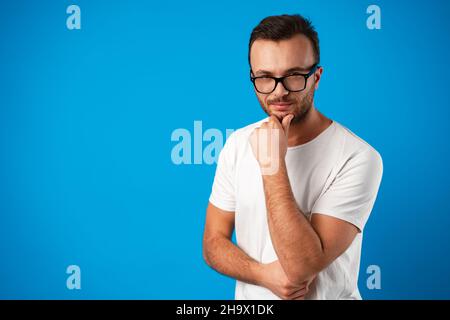 Pensieroso bel maschio indossare occhiali su sfondo blu Foto Stock