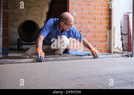 Lavoratori edili che levigano il calcestruzzo al di sopra del sistema radiante del sottopianale. Foto Stock