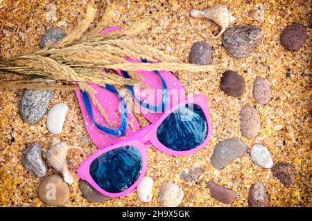 Scena della spiaggia. Cappello di paglia di sole, un paio di sandali flip flop e occhiali da sole adagiati sulle conchiglie di cocaina sul mare sulla spiaggia. Concetto di vacanza Foto Stock