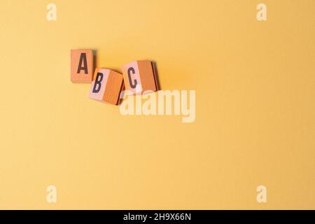 Parola 'ABC' composta da blocchi di lettere in legno su sfondo giallo con uno spazio di copia Foto Stock