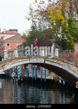 Venezia, Italia - 27 ottobre 2021: Donna che attraversa un ponte su un canale a Venezia (Italia), giorno nuvoloso a fine autunno Foto Stock