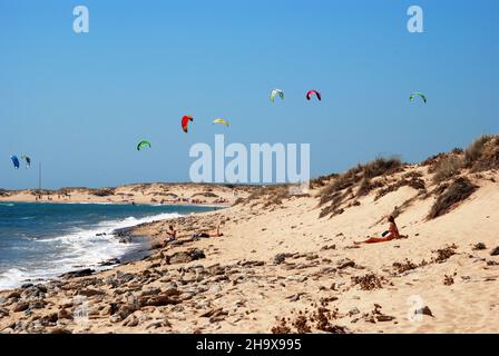 I turisti rilassante sulla spiaggia con kitesurfisti al posteriore, Cabo Trafalgar, la provincia di Cadiz Cadice, Andalusia, Spagna. Foto Stock