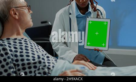 Donna chirurgo che tiene la compressa verde schermo in ospedale reparto per mostrare i risultati del test di esame del paziente malato per iniziare il trattamento di guarigione. Specialista afro-americano che dà consigli sulla salute Foto Stock