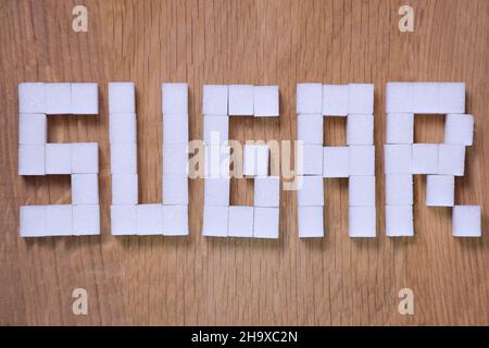 PAROLA DI ZUCCHERO rivestita con raffinati cubetti di zucchero su sfondo marrone legno primo piano Foto Stock