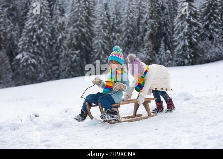 Felice ragazzino e ragazza che slitta in inverno. I bambini che si divertono con gli scivoli da neve in inverno. Figlio e figlia si godono una corsa in slitta. Carta da parati di Capodanno Foto Stock