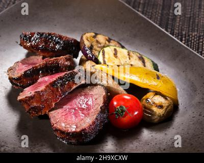 filetto di mignon medio raro servito con verdure grigliate su un piatto su sfondo scuro Foto Stock