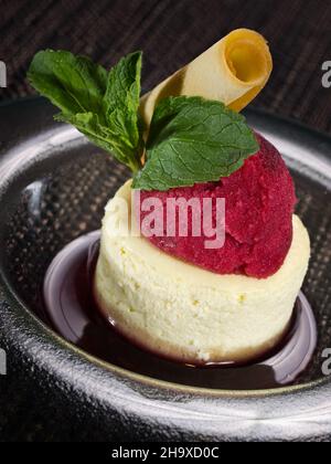 dolce dessert panna cotta in salsa di ciliegia e cucchiaio di sorbetto al ciliegia, foto verticale su sfondo scuro Foto Stock