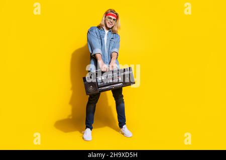 Foto di simpatico ragazzo giovane vestito denim camicia sorridente ballare tenendo boom box isolato colore giallo sfondo Foto Stock