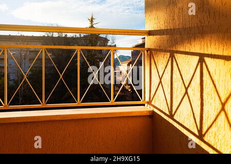 Angolo di un balcone formato da una ringhiera e il muro. Il sole splende da sinistra e l'ombra del traliccio è gettata sul muro. T Foto Stock