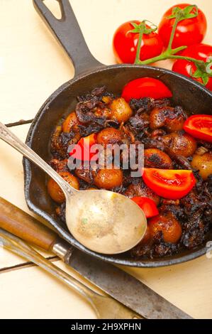 Baby seppie arrostite in padella di ferro con pomodori e cipolle su tavola in legno rustico Foto Stock