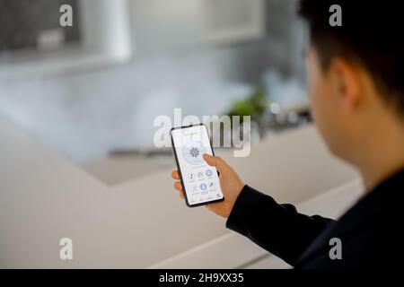 Uomo che utilizza l'app della casa intelligente sullo smartphone Foto Stock