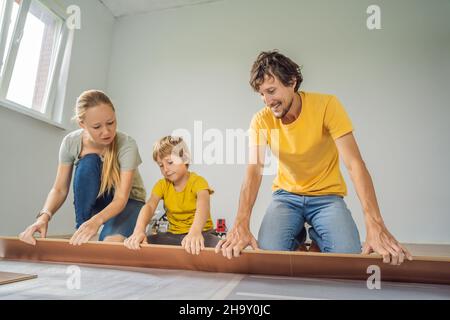 Famiglia felice che installa il nuovo pavimento in laminato di legno su un pavimento caldo della pellicola. Impianto di riscaldamento a infrarossi sotto il pavimento in laminato Foto Stock