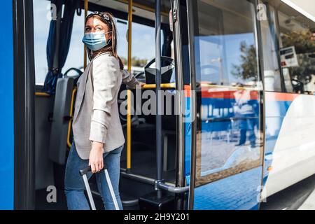 Giovane donna con bagaglio e maschera di protezione imbarco per l'autobus di Faro, Portogallo Foto Stock